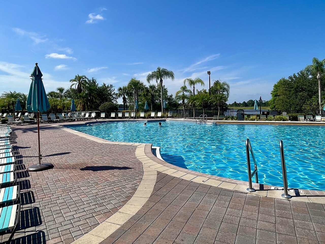 A resort swimming pool lined with palm trees and umbrellas