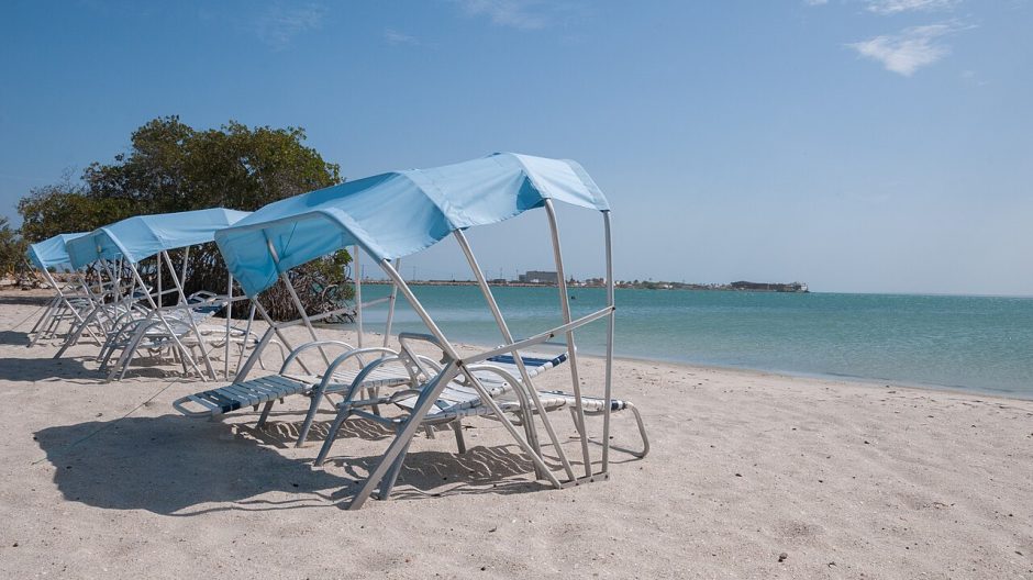 Shaded lounge chairs on a quiet sandy beach with calm blue water in the background