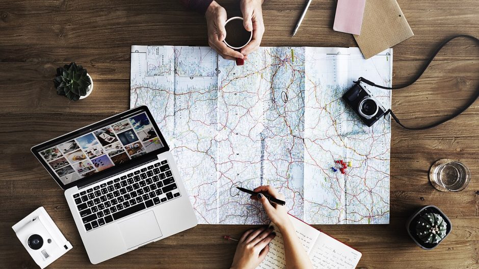 Two people planning a trip with a paper map, a laptop and coffee on a wooden table