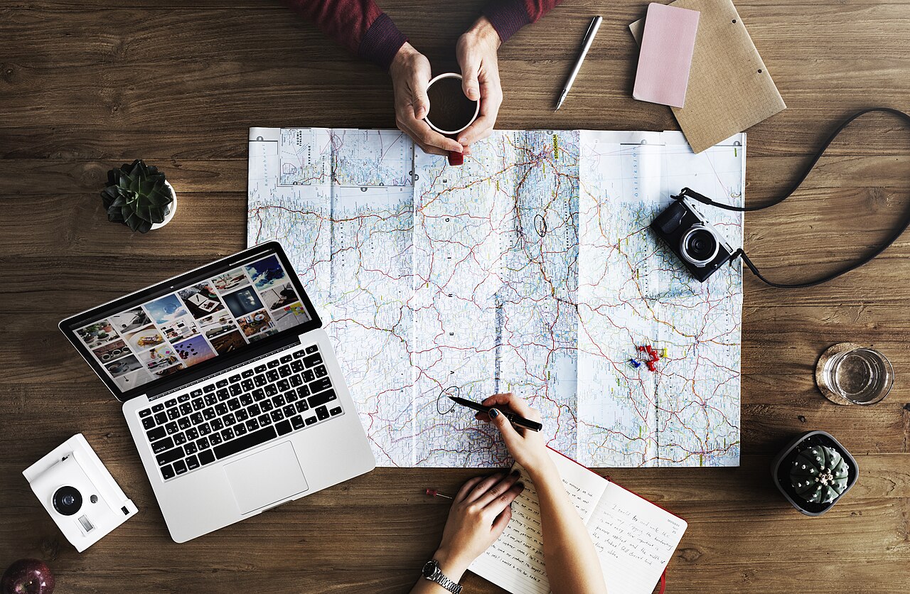 Two people planning a trip with a paper map, a laptop and coffee on a wooden table