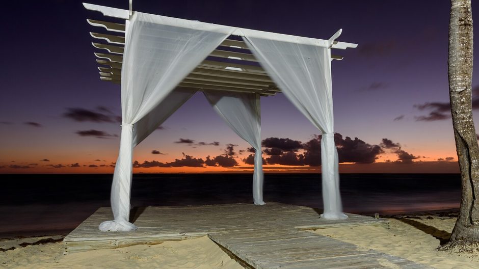 A wedding canopy draped in white fabric on a beach boardwalk at dusk